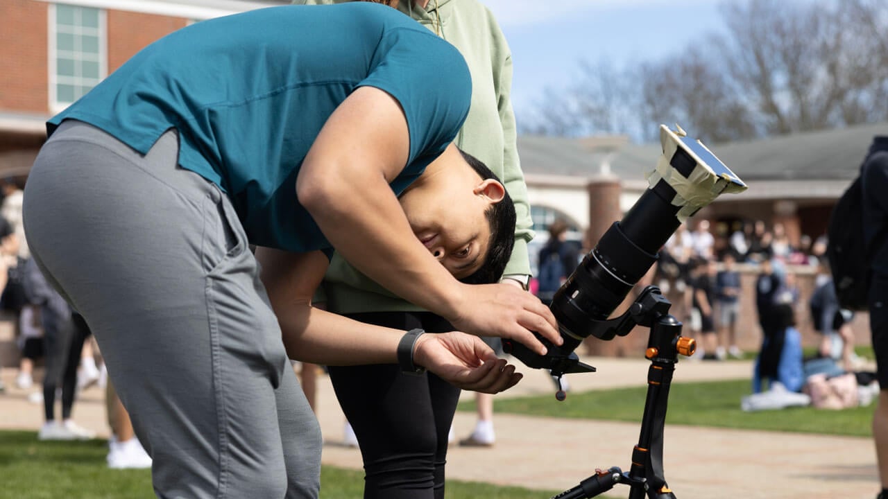 A student looks through their camera at the solar eclipse.