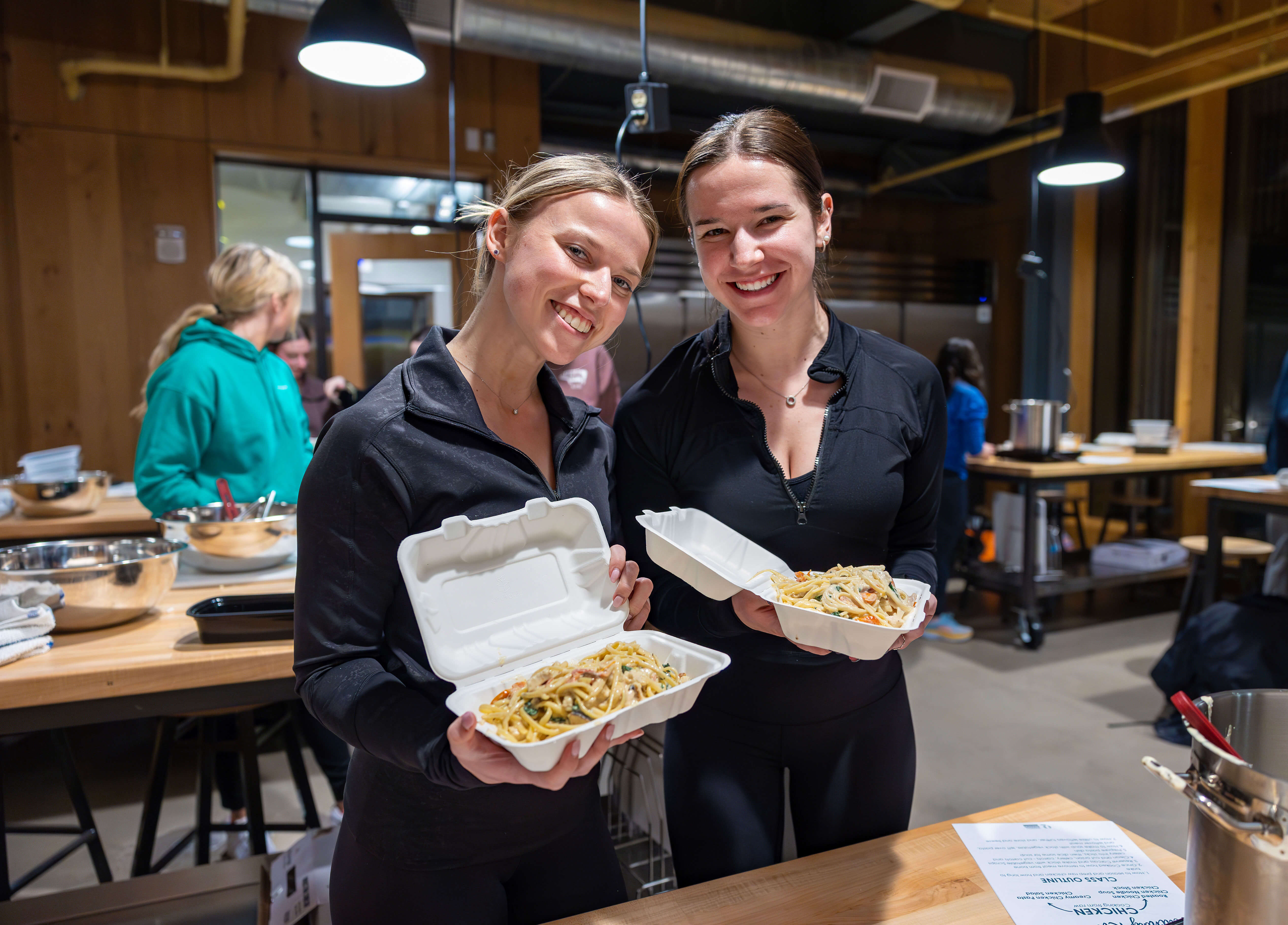 2 Girls smiling holding up pasta in the adulting meal prep for beginners class