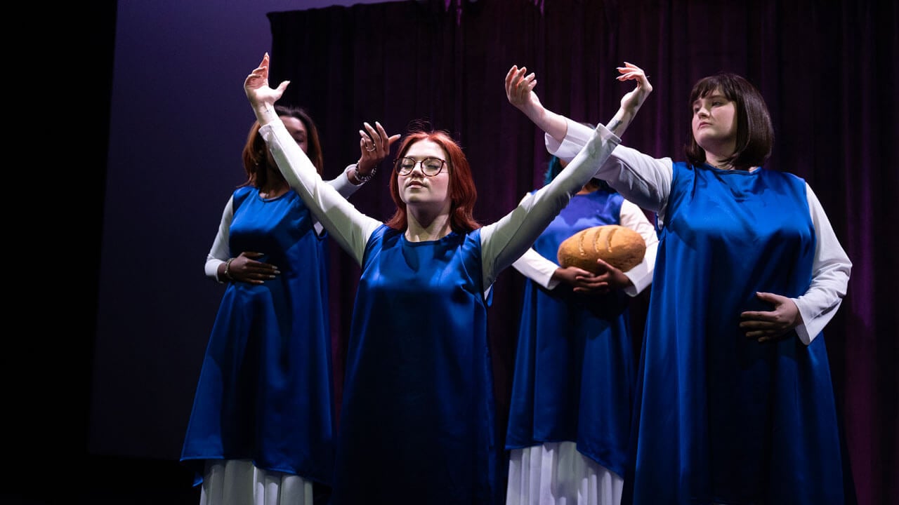 One quinnipiac student holds a loaf of bread as others have their hand raised in Quinnipiac spring play