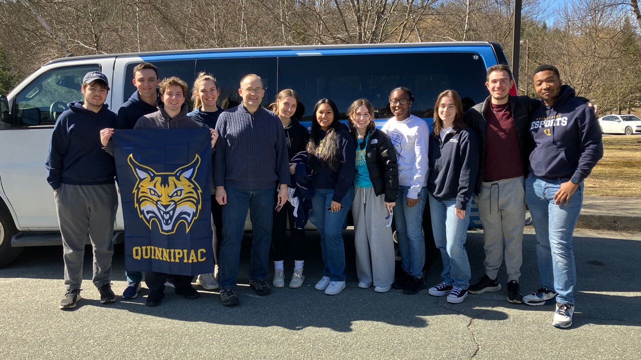 A group of students and professor hold up a Quinnipiac flag.