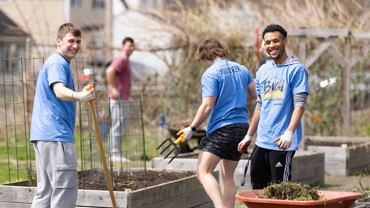Students give back to the community holding rakes and working in a garden