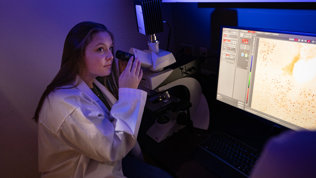 A female student looking at a screen from a microscope