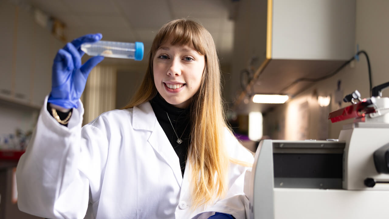 A female student hoping up a plastic tube smiling at the camera