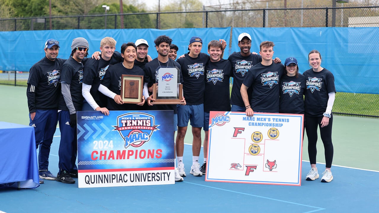 The men's tennis team stand with large posters and trophies.