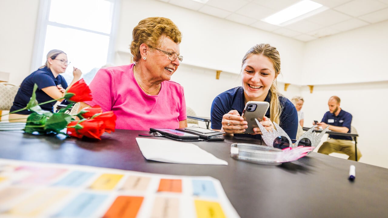 A student helping an older woman work an iPhone