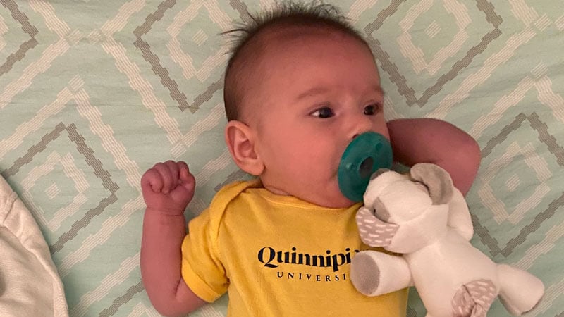 Buckley baby in a Quinnipiac shirt lies on a bed