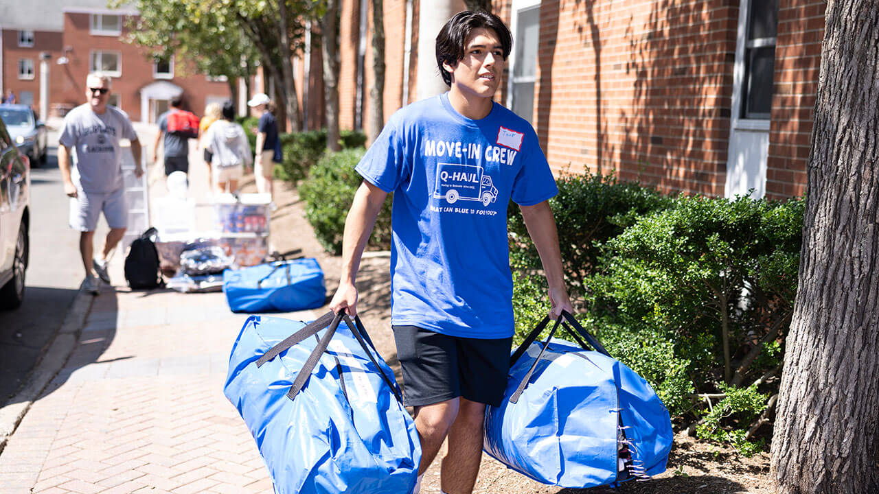 A student carries duffle bags into the residence hall