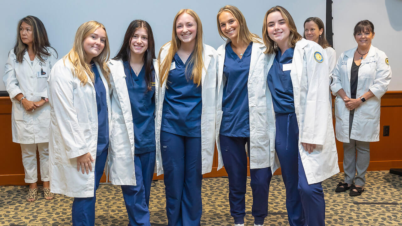 five nursing students pose together and show off their new white coats