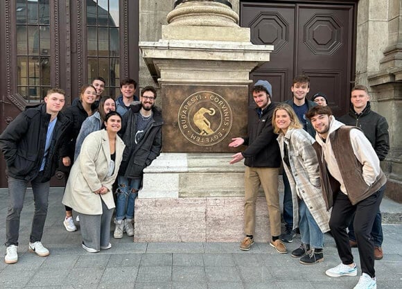 A group of student posing in front of Corvinus emblem
