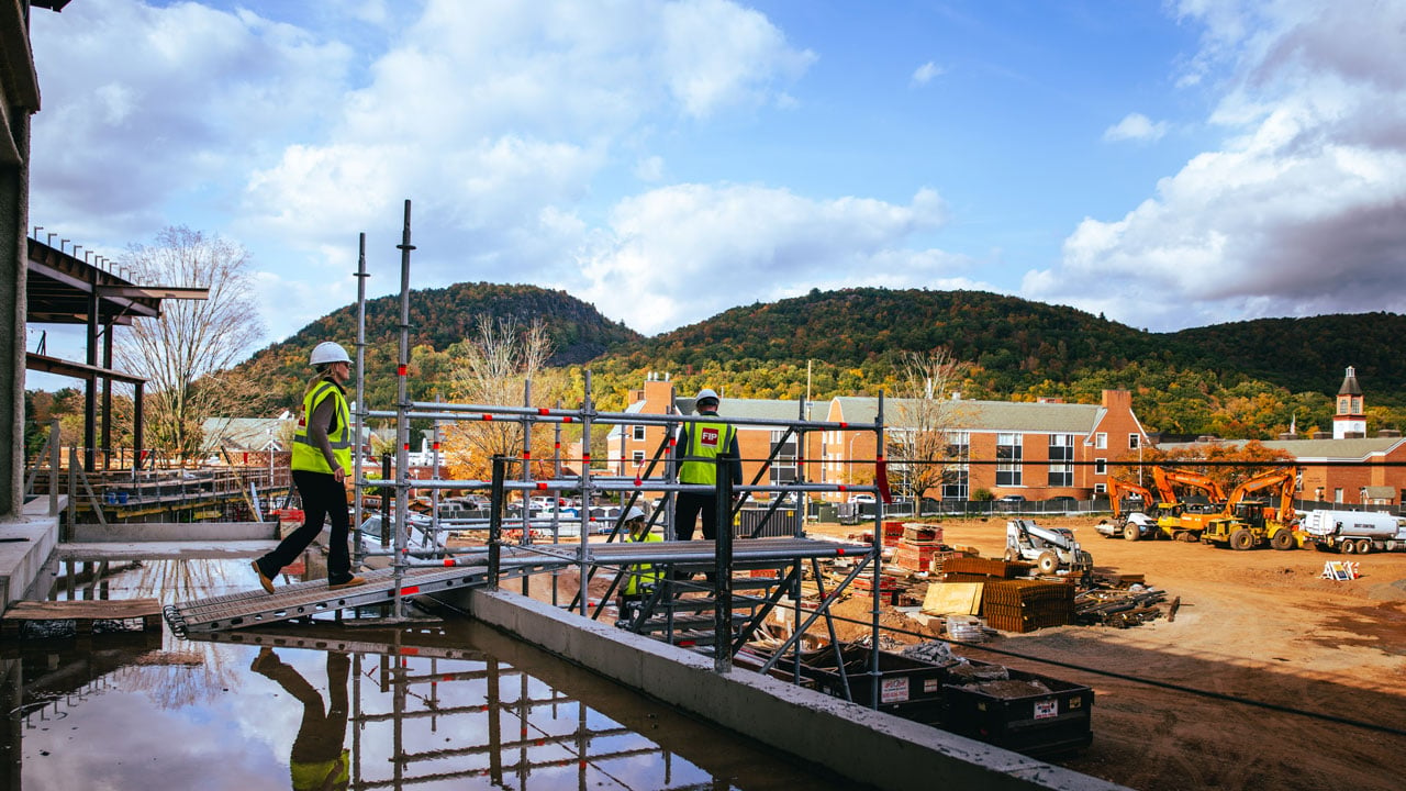 Construction workers walk across a platform on the south quad site.