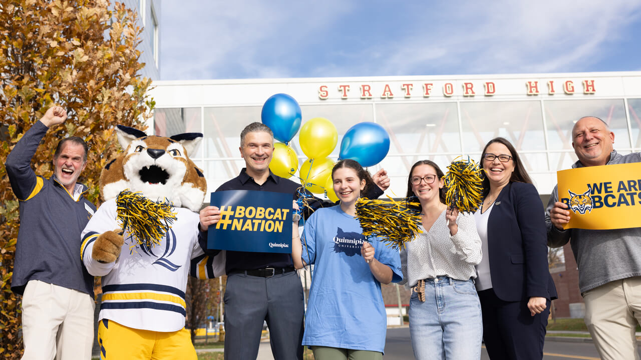 A newly admitted student celebrates with her family and Quinnipiac staff and mascot outside school