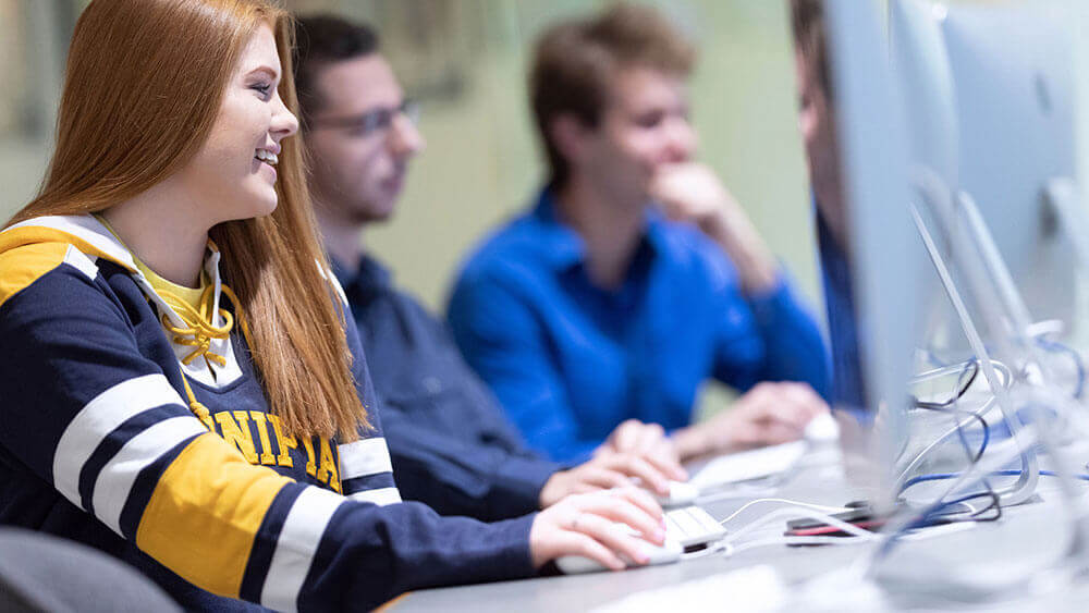 Three Quinnipiac students work on computers in a communications classroom