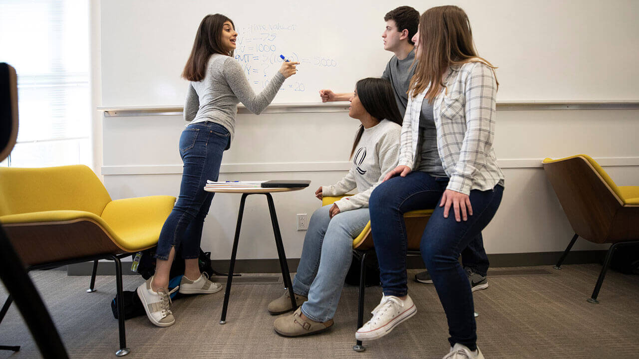 One student writes on a white board while three other students look on