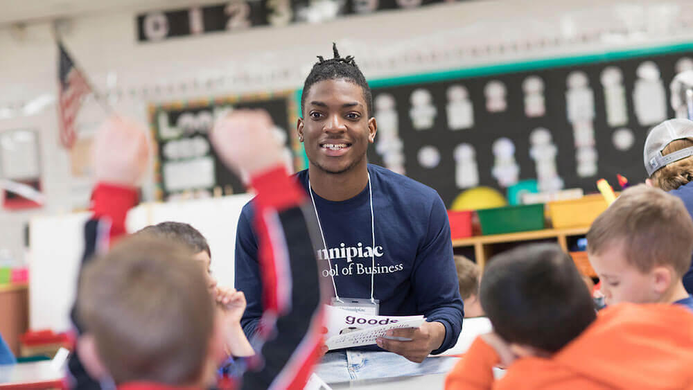 A business student wearing a Quinnipiac shirt reads to elementary schoolers