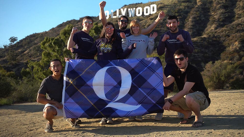 Quinnipiac students pose in front of the Hollywood sign holding a large Q flag