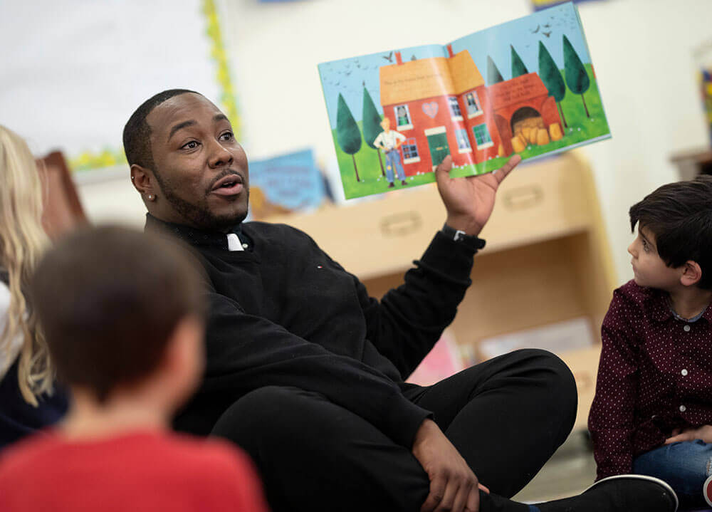 A School of Education graduate student reads a colorful picture book out loud to a group of elementary students