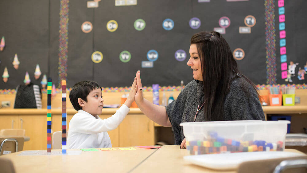 Education alumni Marisa Laudano hi-fives a kindergartner in a classroom