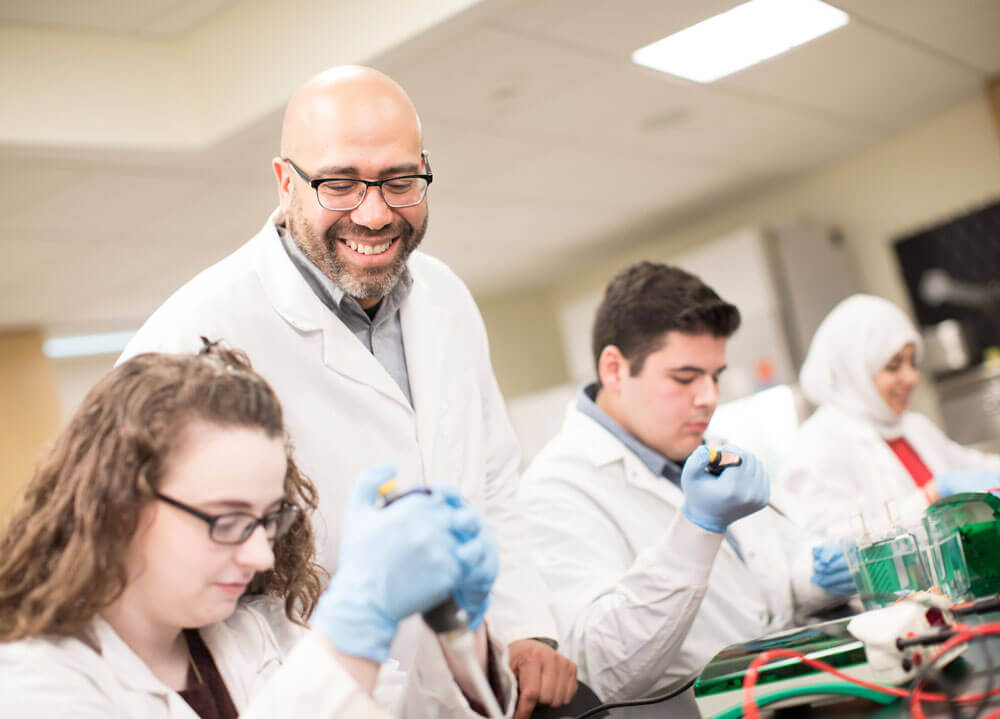 Professor smiles at students as they complete a lab