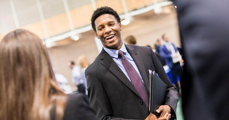 A student wearing a suit smiles as he talks to someone during a career fair