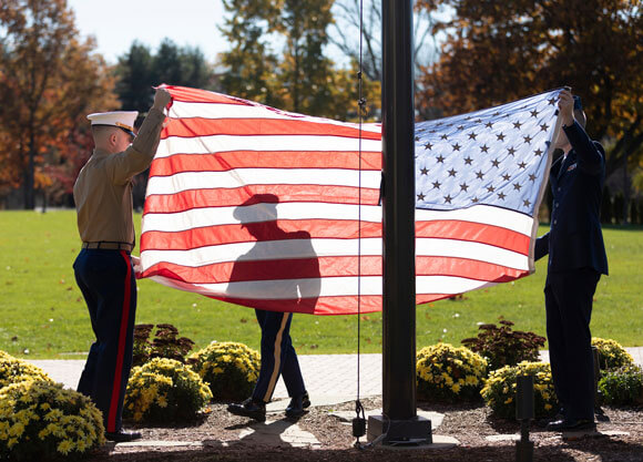 Three student veterans raise an American flag during a ceremony
