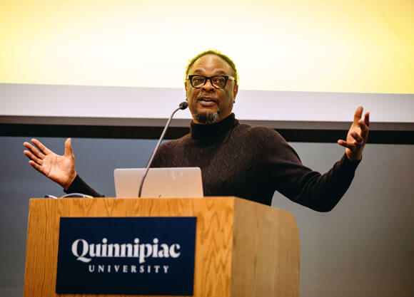 Lawrence Ross speaking in front of a podium with Quinnipiac University
