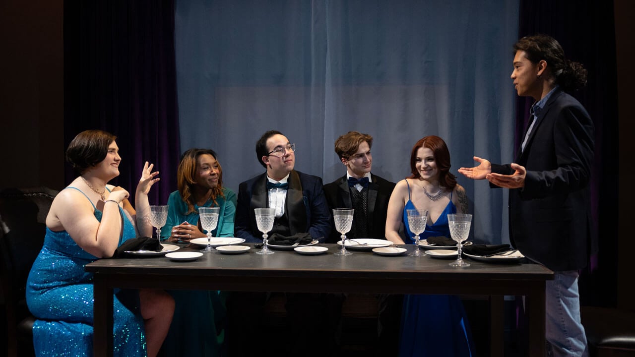 Quinnipiac students sitting at a table acting in the spring play
