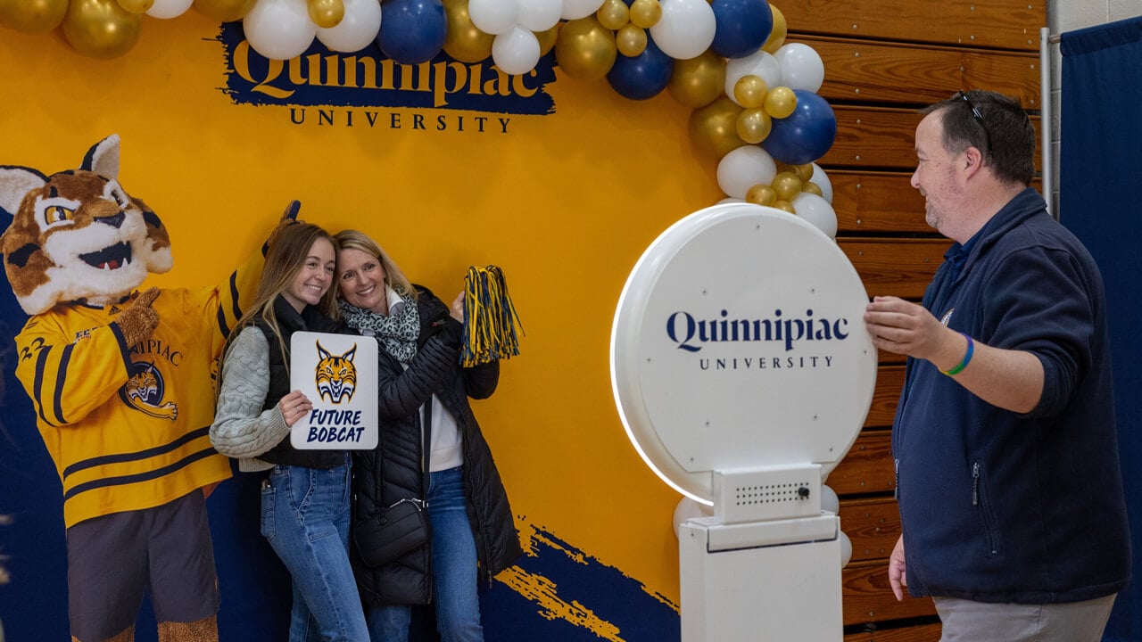 A newly admitted student poses in a photo booth with Boomer and a family member