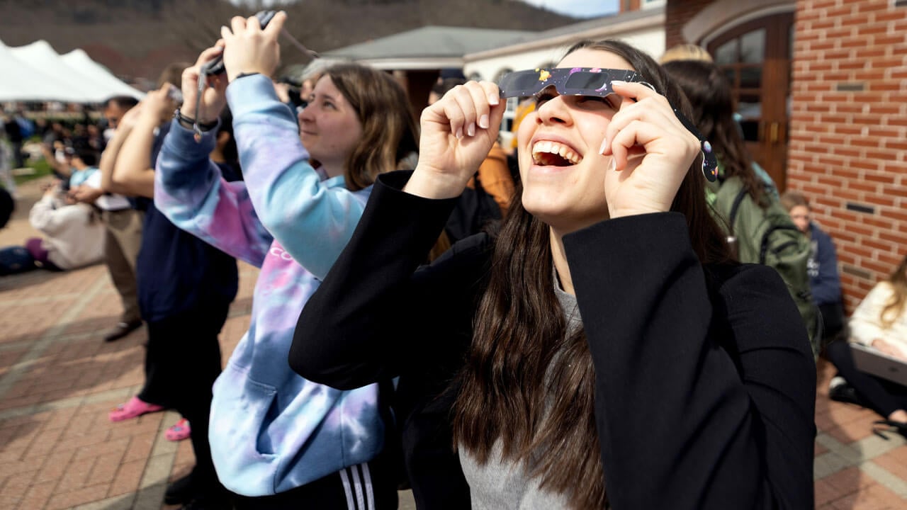 A student smiles big while looking through solar eclipse glasses.