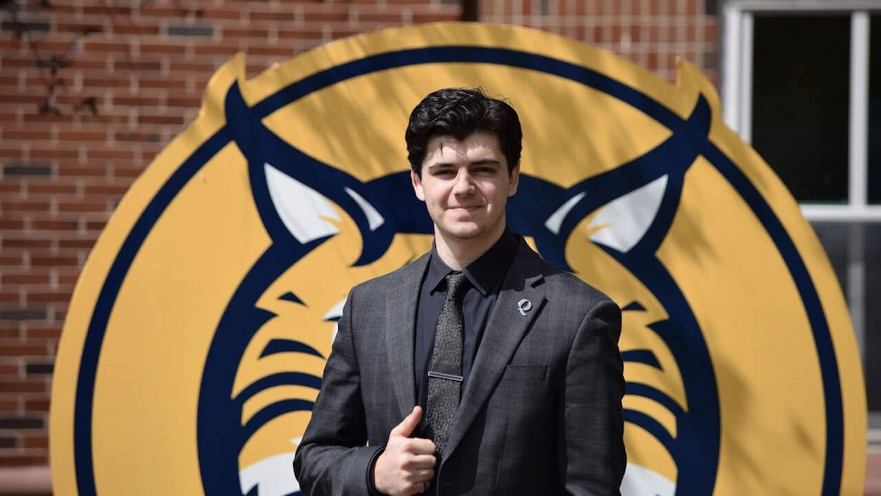 Jake Cedor wearing a suit and smiling outside in front of a bobcat sign.