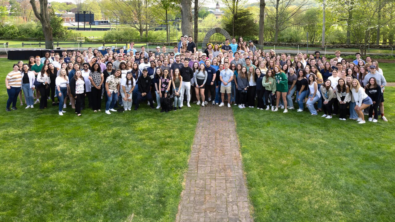 Members of the Quinnipiac Class of 2024 pose for a group photo with the library clocktower behind