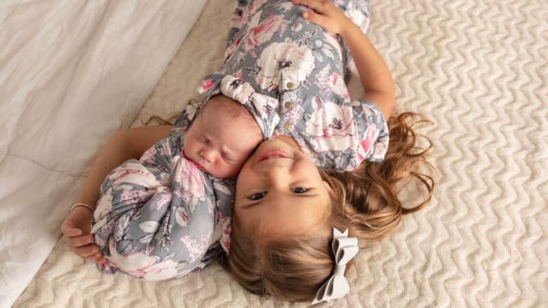 Baby Rivera and her sister wear matching outfits and snuggle on a bed