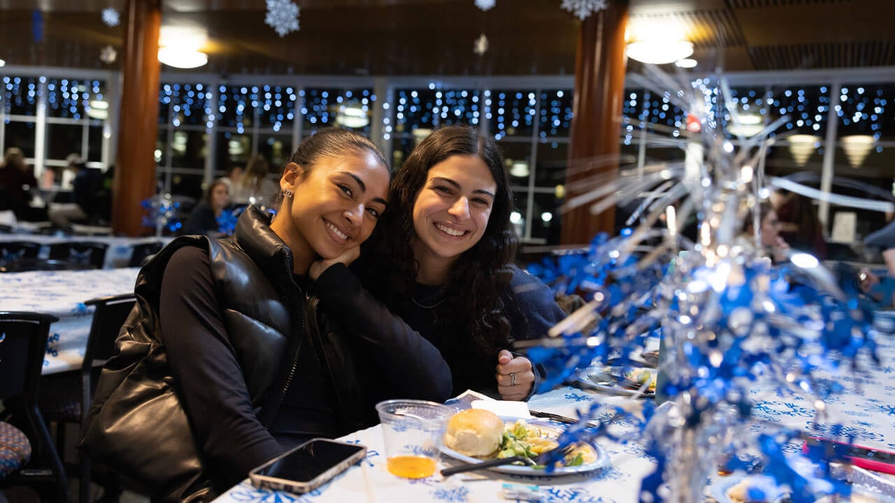 Two students sitting at holiday decorated table with food and smiling