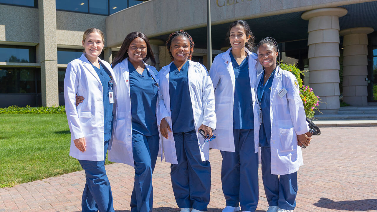 five nursing students pose wearing their white coats outside