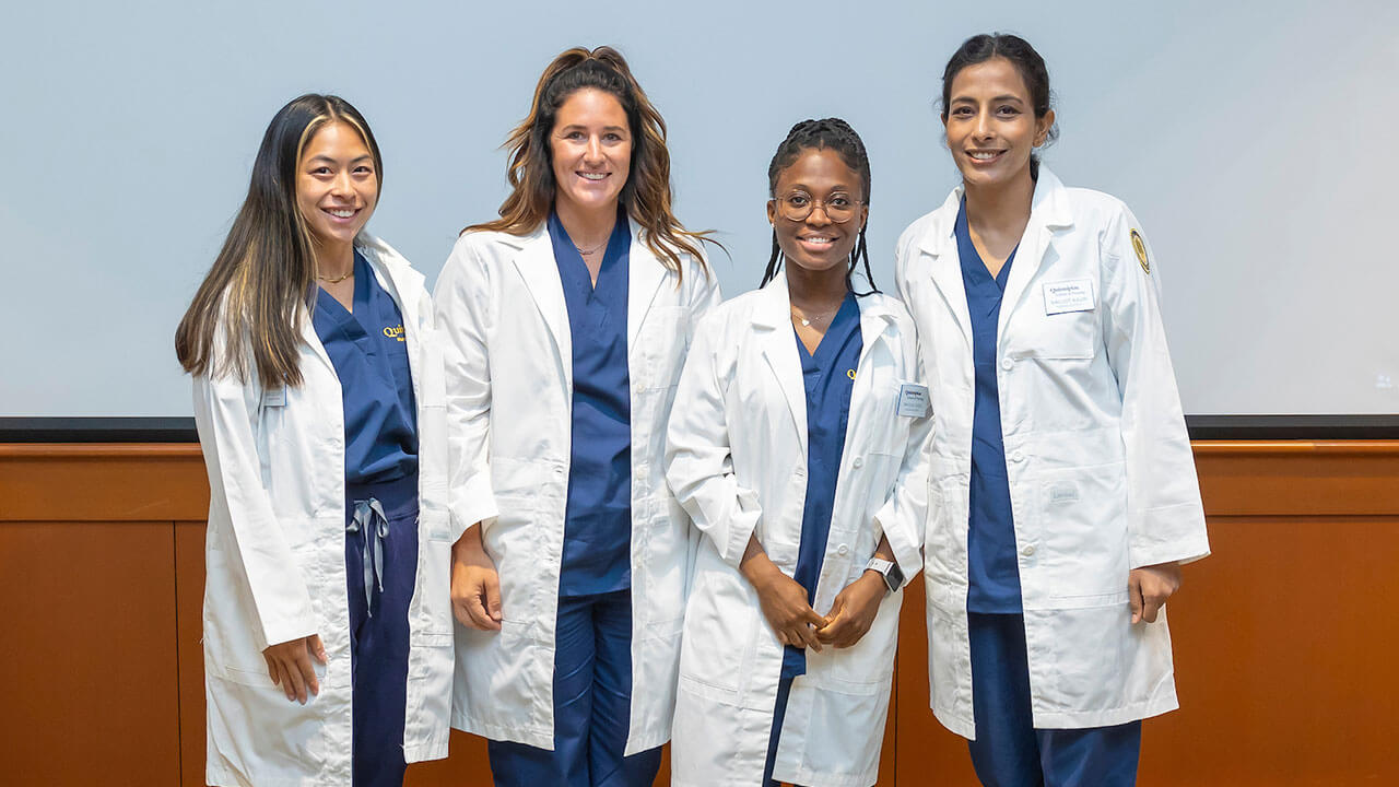 four nursing students pose smiling wearing their white coats