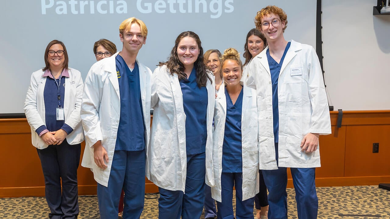 four nursing students pose smiling with their advisors wearing white coats