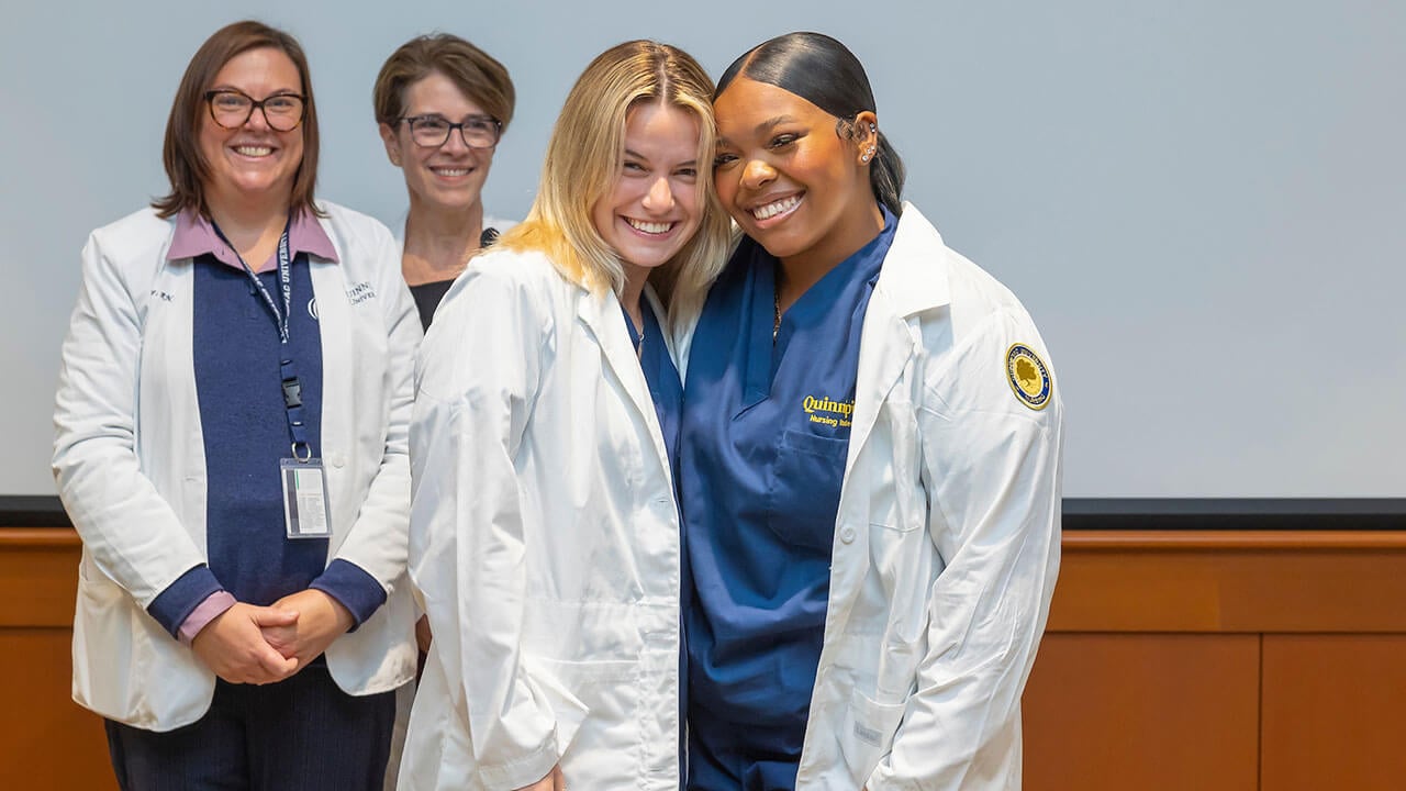 two nursing students smile excitedly with their new white coats