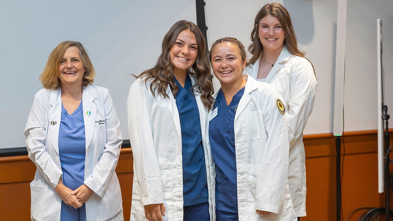 two nursing students pose smiling in front of their advisors
