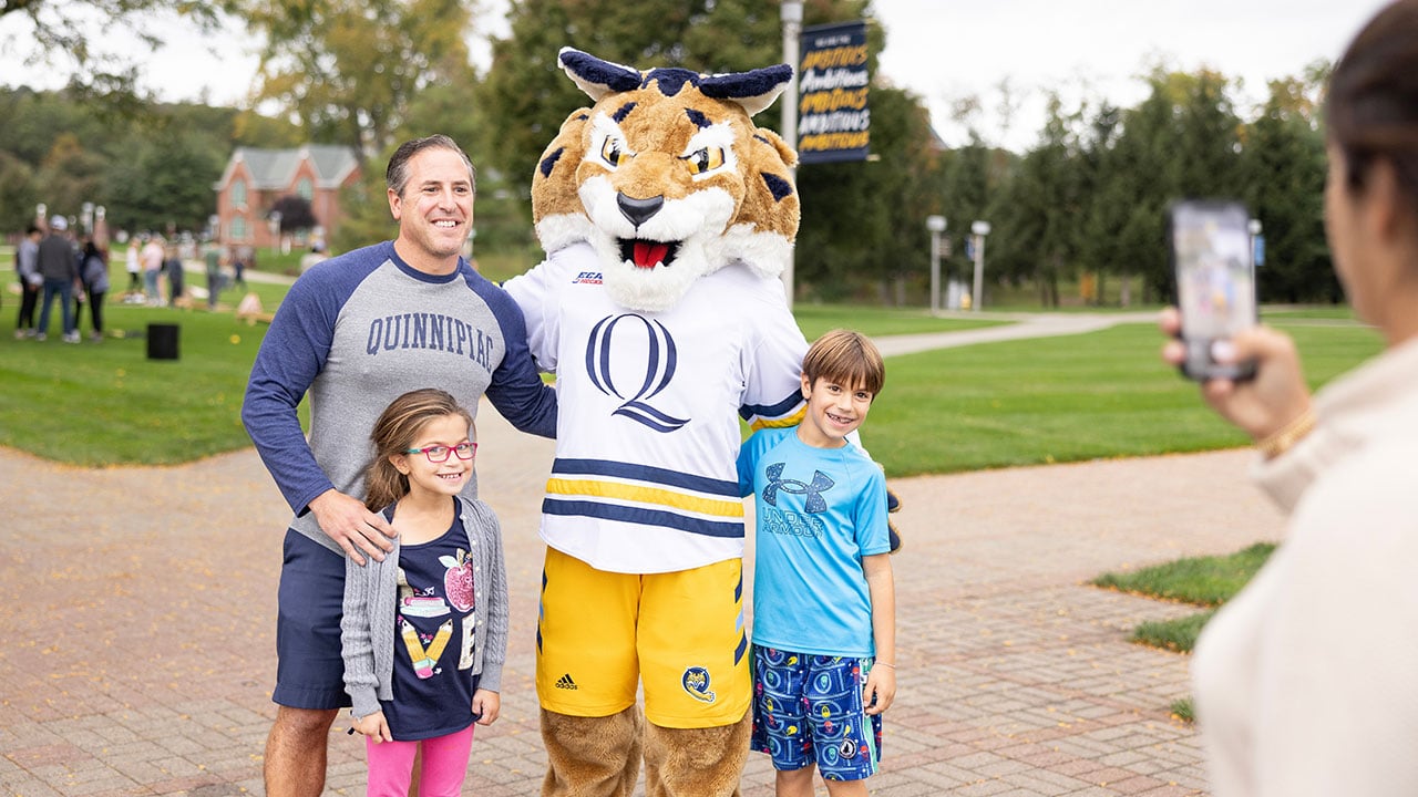 An alumnus stands with his family and Boomer on the Quad.