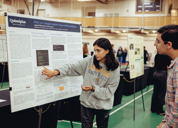 A student points to her academic poster as she presents her research to an Exploratorium attendee.