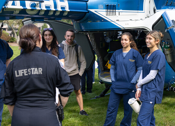 Several health sciences students talk with EMTs outside a Life Star helicopter