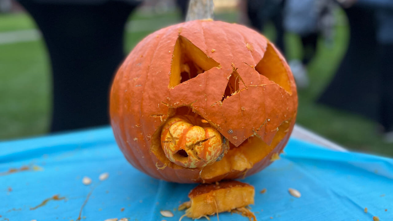 A large pumpkin is carved like it is biting a smaller pumpkin.