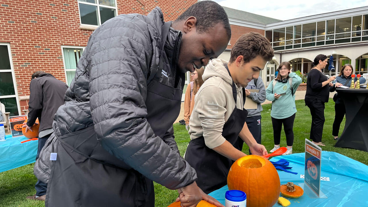 A doctor and student carving pumpkins together at a table