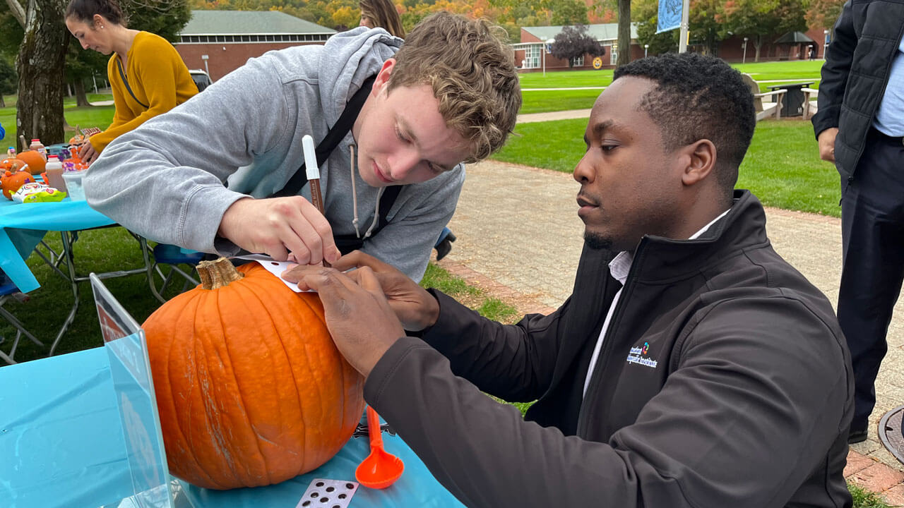 A doctor and student tracing a design onto a pumpkin to prepare for carving