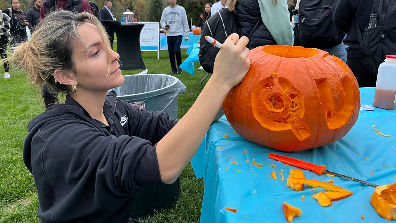 A female student carves a pumpkin with the letters Q and U
