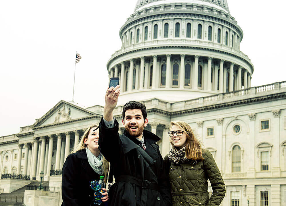 Three students take a selfie in front of the Capitol building in Washington, D.C.
