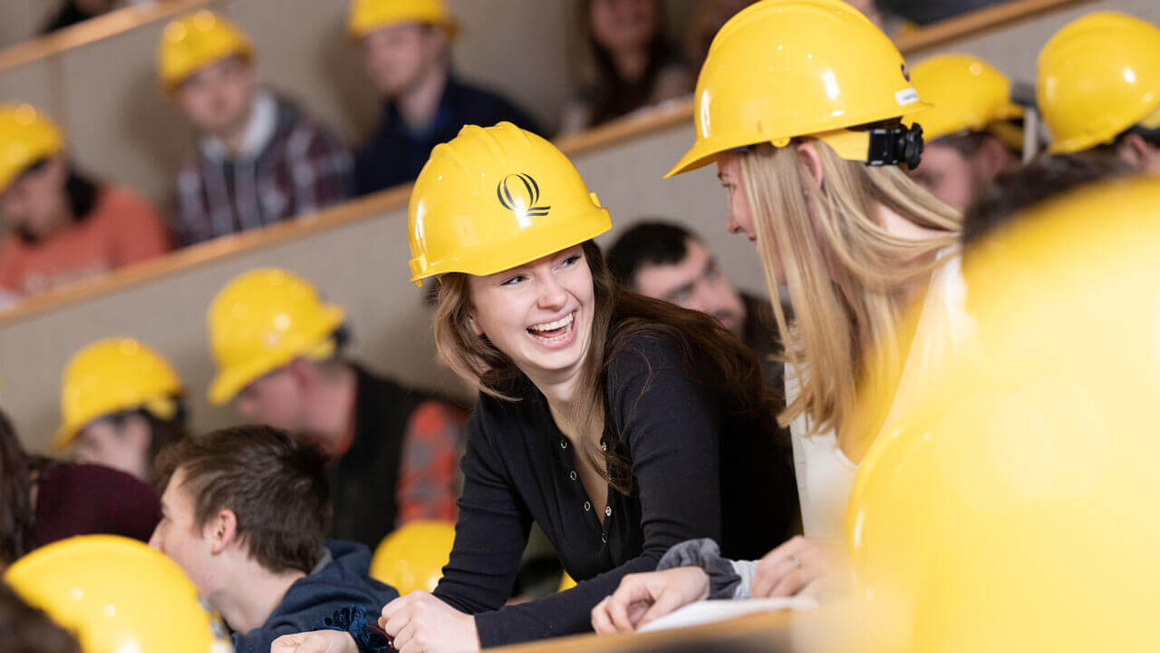 Two students smiling at each other while wearing Quinnipiac-branded hard hats