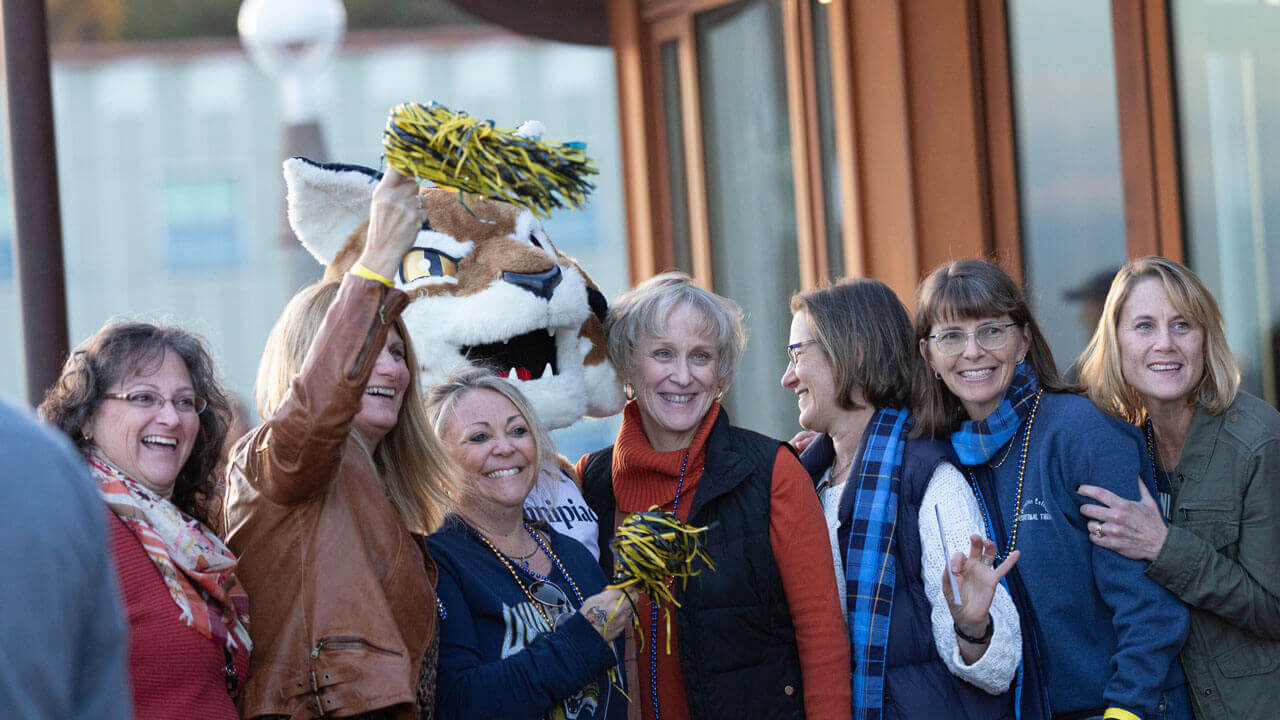 Several alumnae smile for a photo with Boomer the mascot at Alumni Weekend event
