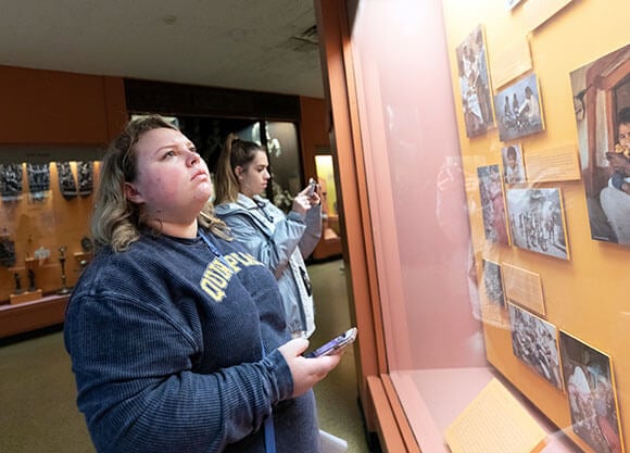 Rachel Houlihan stands with another student looking at a photos and information behind glass at a museum exhibit.
