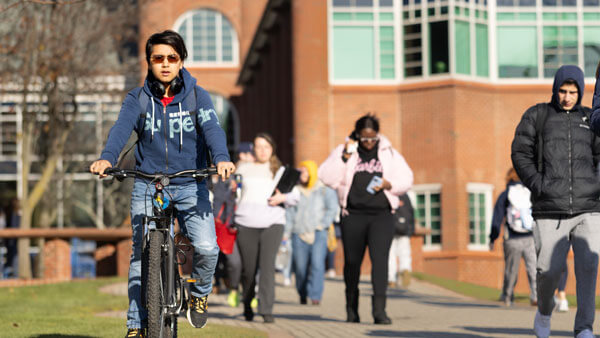 Student riding a bike in front of School of Communications and Engineering at Quinnipiac